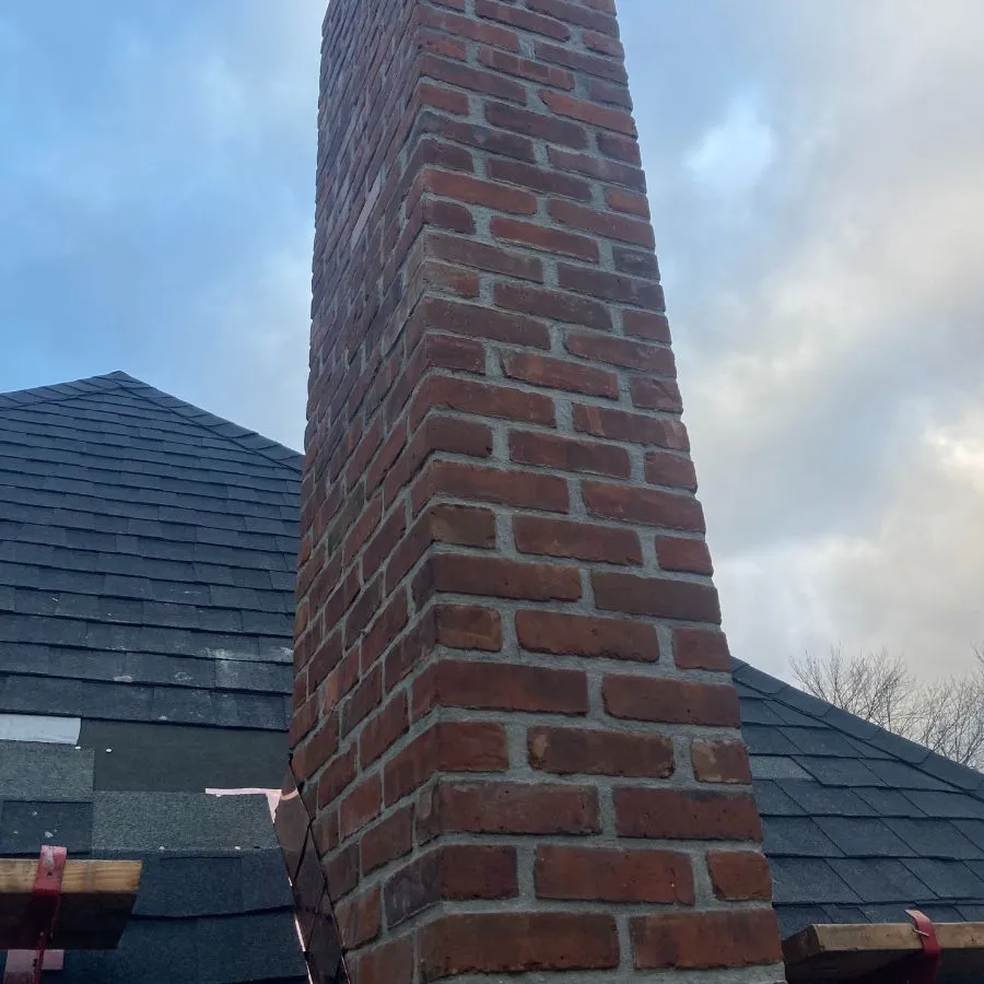 Tall brick chimney on asphalt roof during flashing installation
